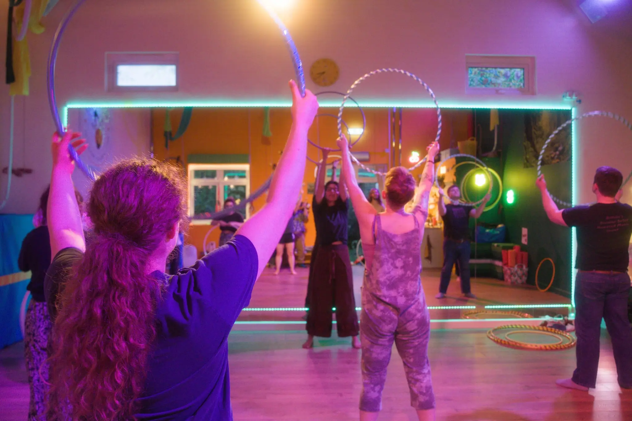 Workshop attendees reaching up with their hoops in a LED-lit studio